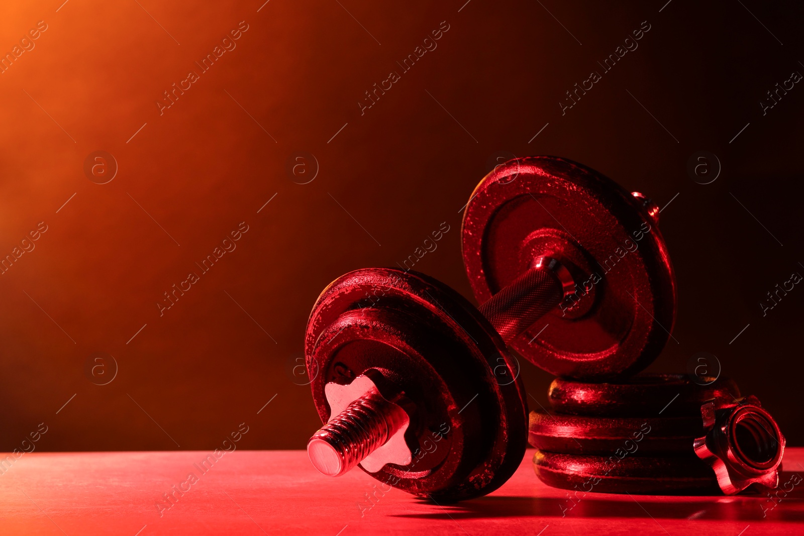 Photo of Barbell and parts of one on table in color lights. Space for text