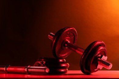 Photo of Barbell and parts of one on table in color lights. Space for text