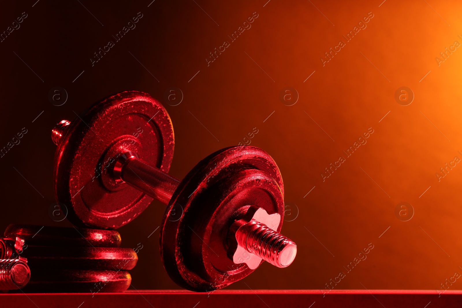 Photo of Barbell and parts of one on table in color lights. Space for text