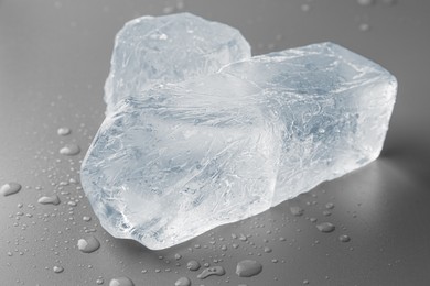 Photo of Pieces of clear ice and water drops on light grey table, closeup