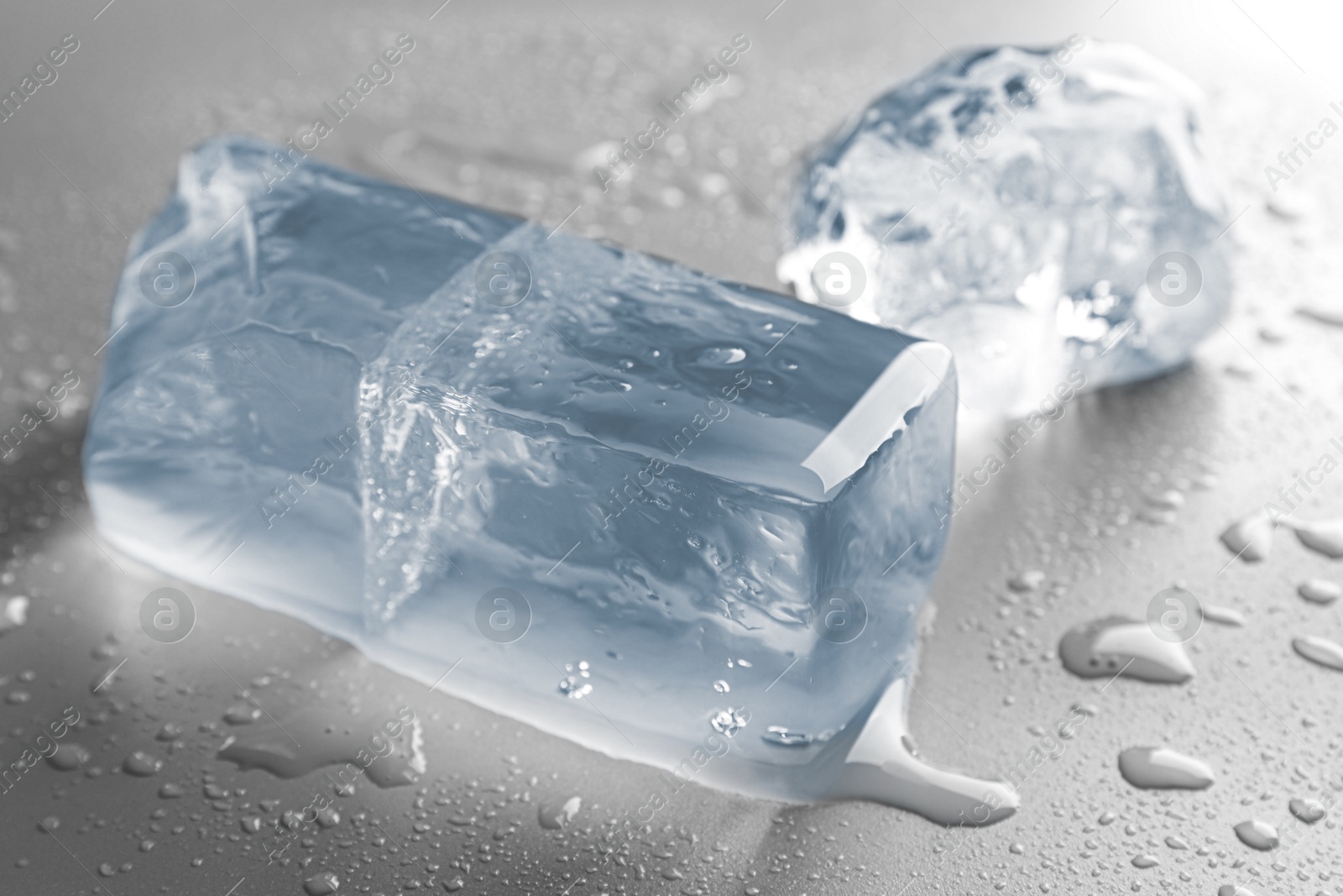 Photo of Pieces of clear ice and water drops on light grey table