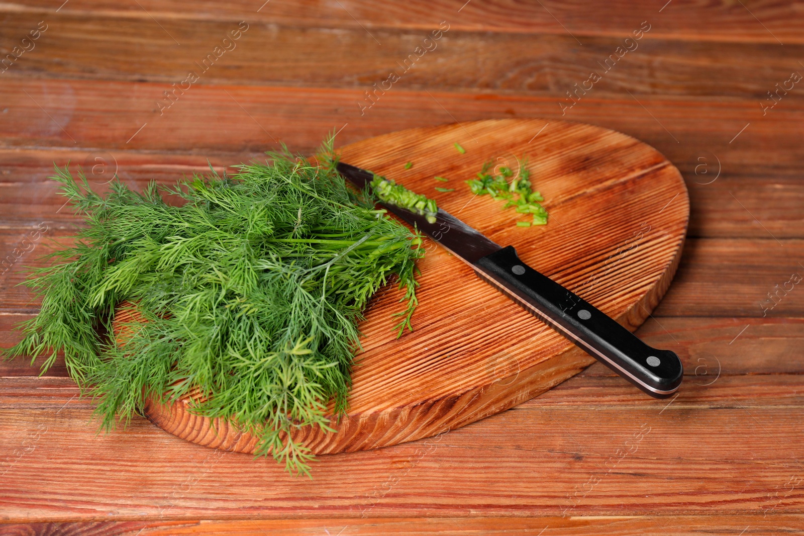 Photo of Sprigs of fresh green dill and knife on wooden table