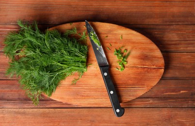 Photo of Sprigs of fresh green dill and knife on wooden table, top view