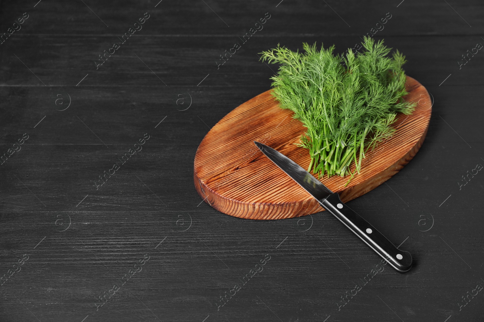 Photo of Sprigs of fresh green dill and knife on black wooden table, space for text