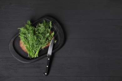 Photo of Sprigs of fresh green dill and knife on black wooden table, top view. Space for text