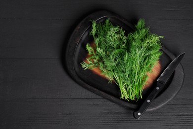 Photo of Sprigs of fresh green dill and knife on black wooden table, top view. Space for text