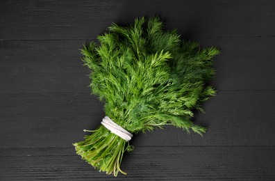 Photo of Bunch of fresh green dill on black wooden table, top view