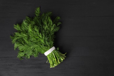 Photo of Bunch of fresh green dill on black wooden table, top view. Space for text