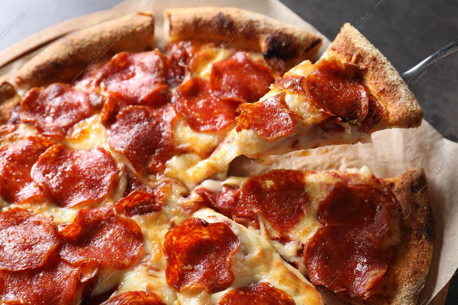 Photo of Taking piece of tasty pepperoni pizza at grey table, closeup