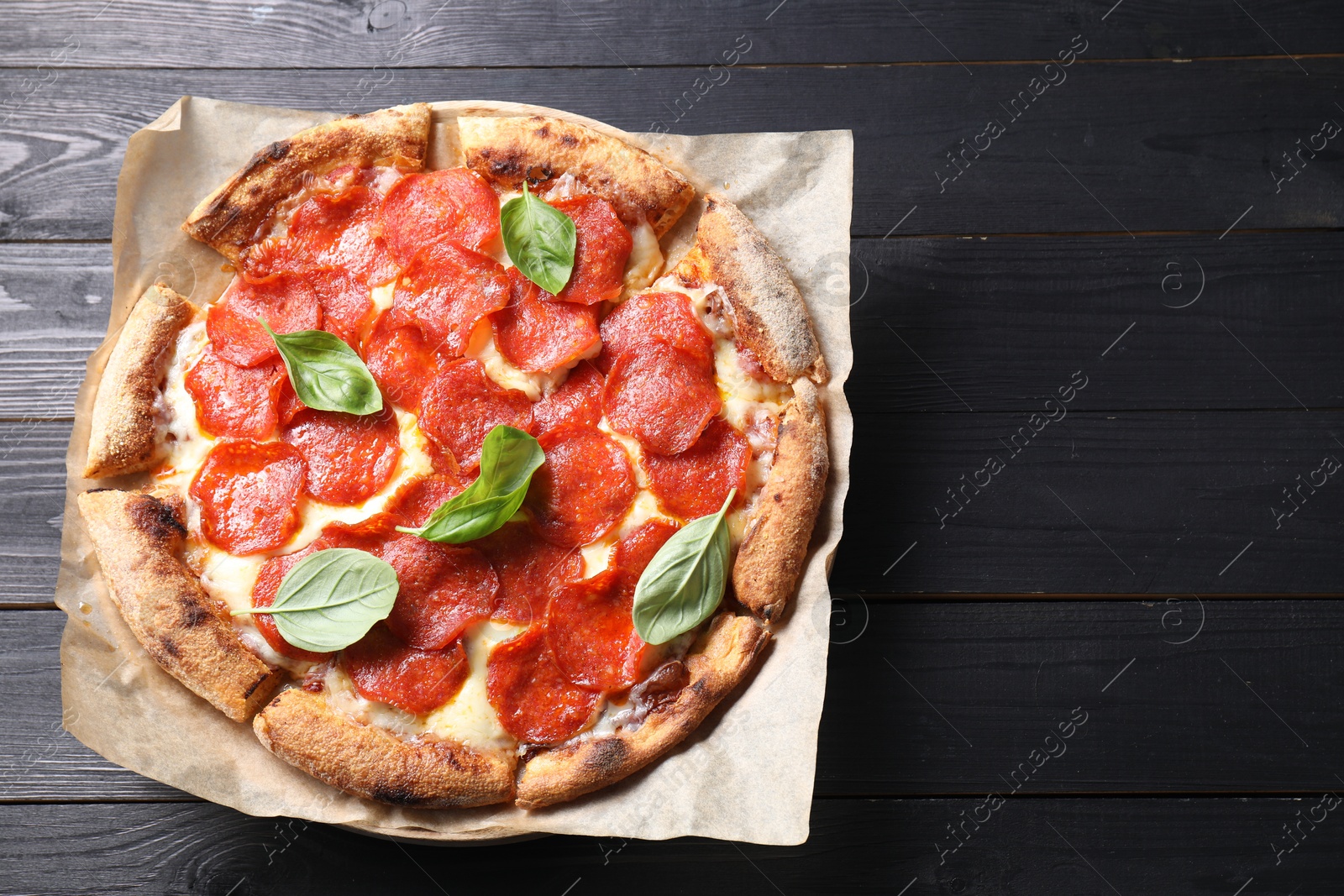 Photo of Tasty pepperoni pizza with basil on black wooden table, top view. Space for text