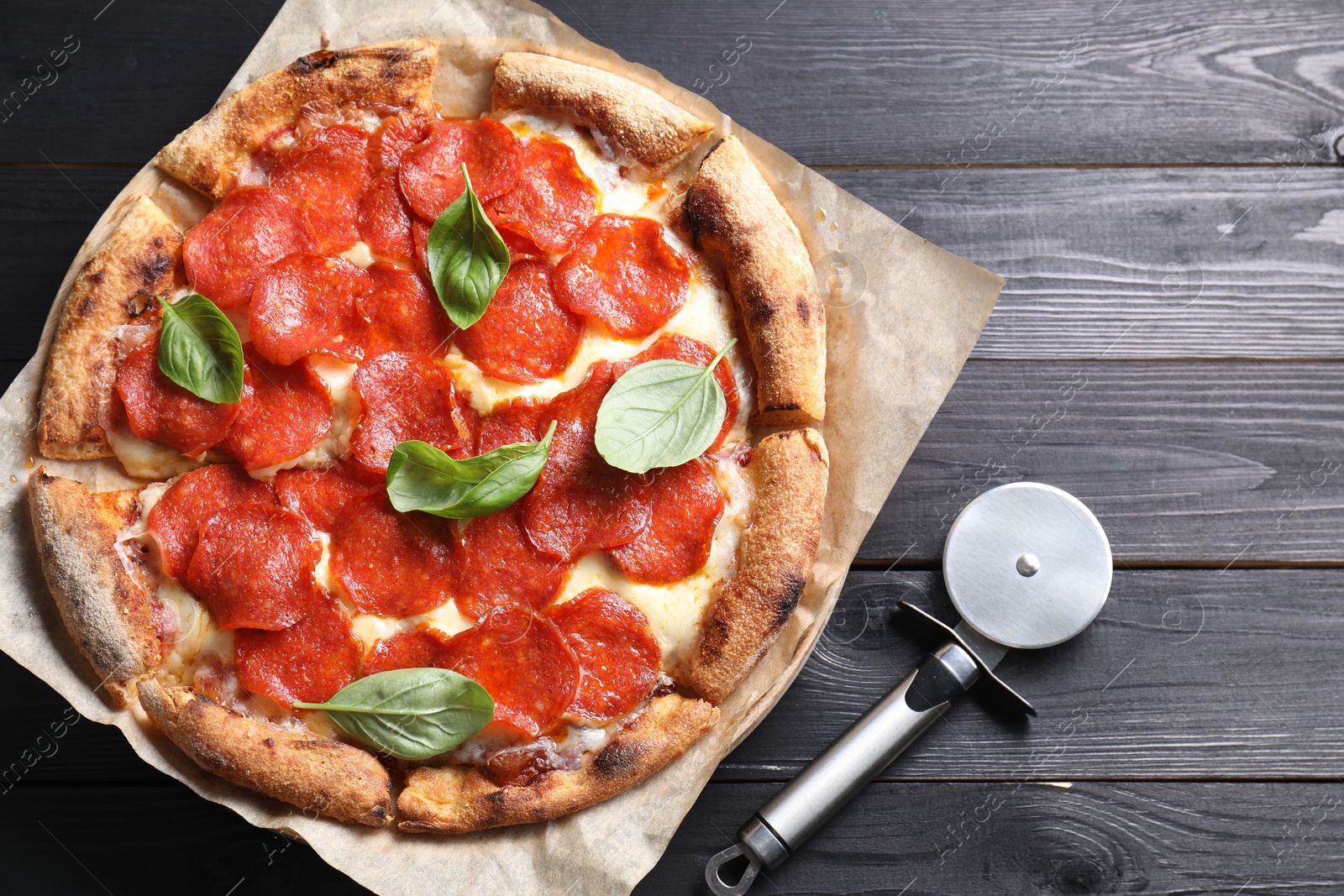 Photo of Tasty pepperoni pizza with basil and cutter on black wooden table, top view. Space for text