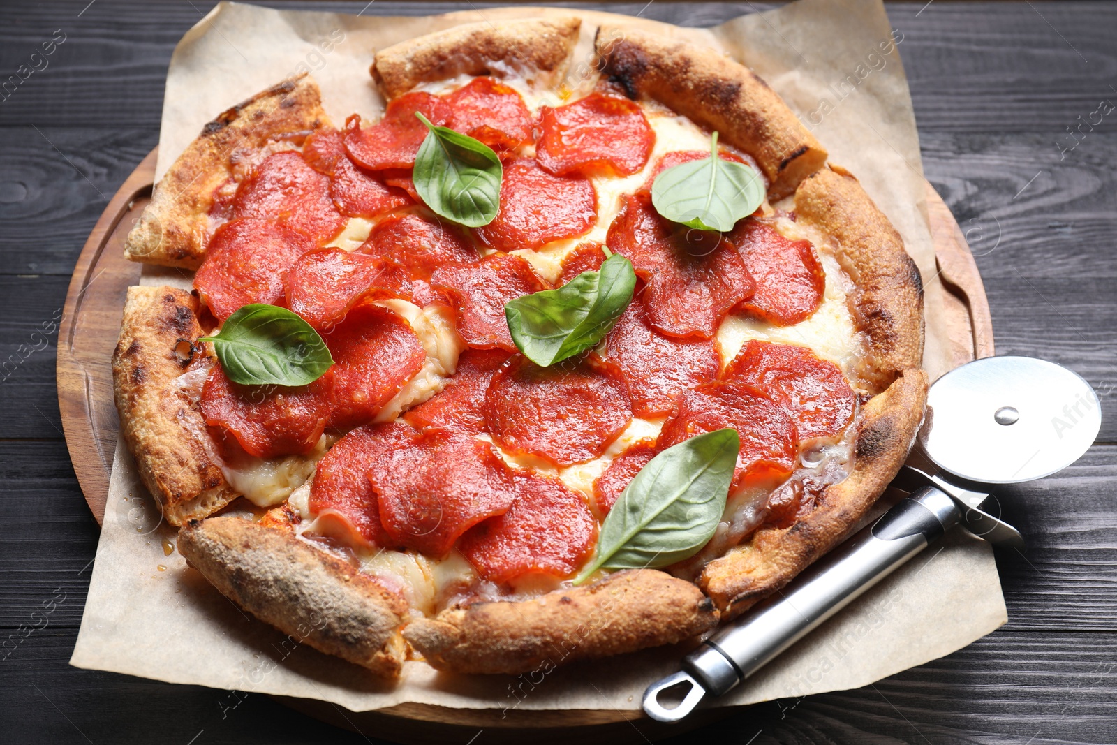 Photo of Tasty pepperoni pizza with basil and cutter on black wooden table