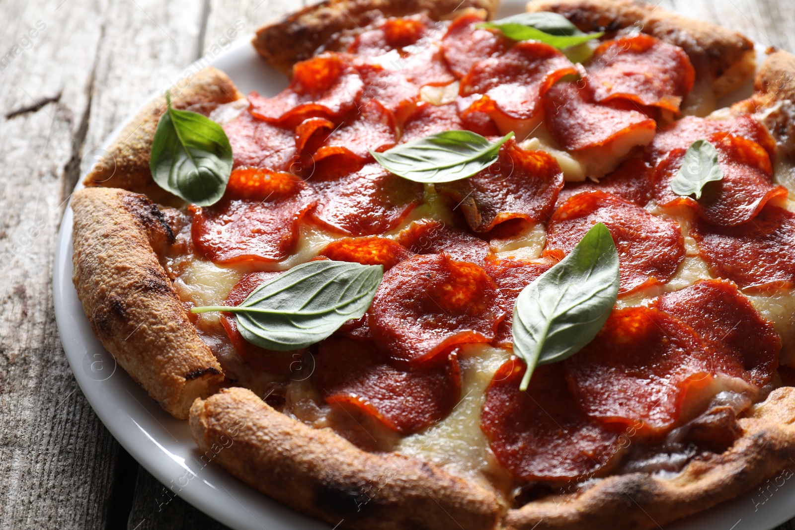 Photo of Tasty pepperoni pizza with basil on wooden table, closeup