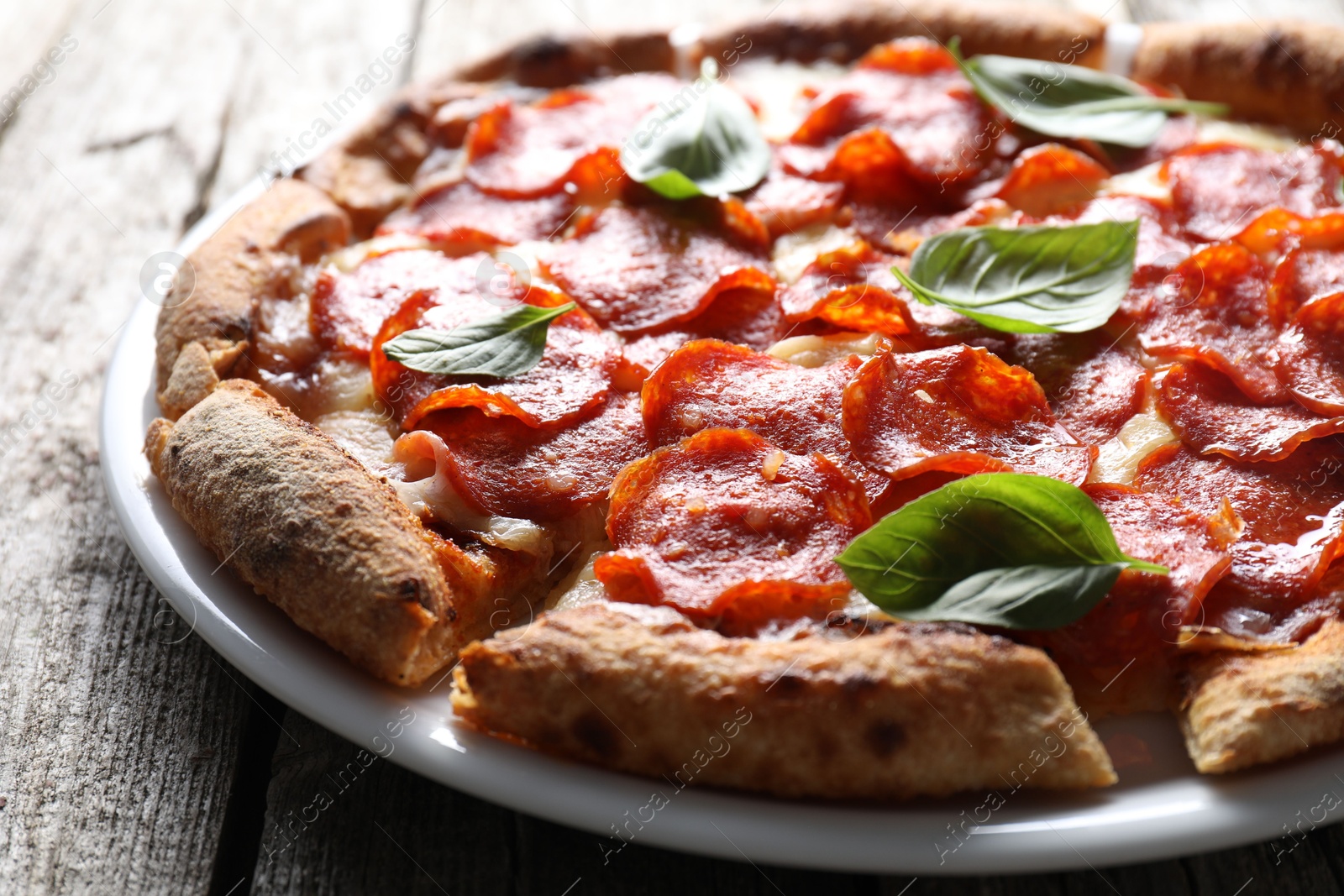 Photo of Tasty pepperoni pizza with basil on wooden table, closeup