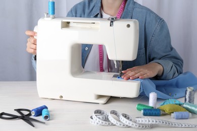 Photo of Seamstress working with sewing machine at white wooden table indoors, closeup