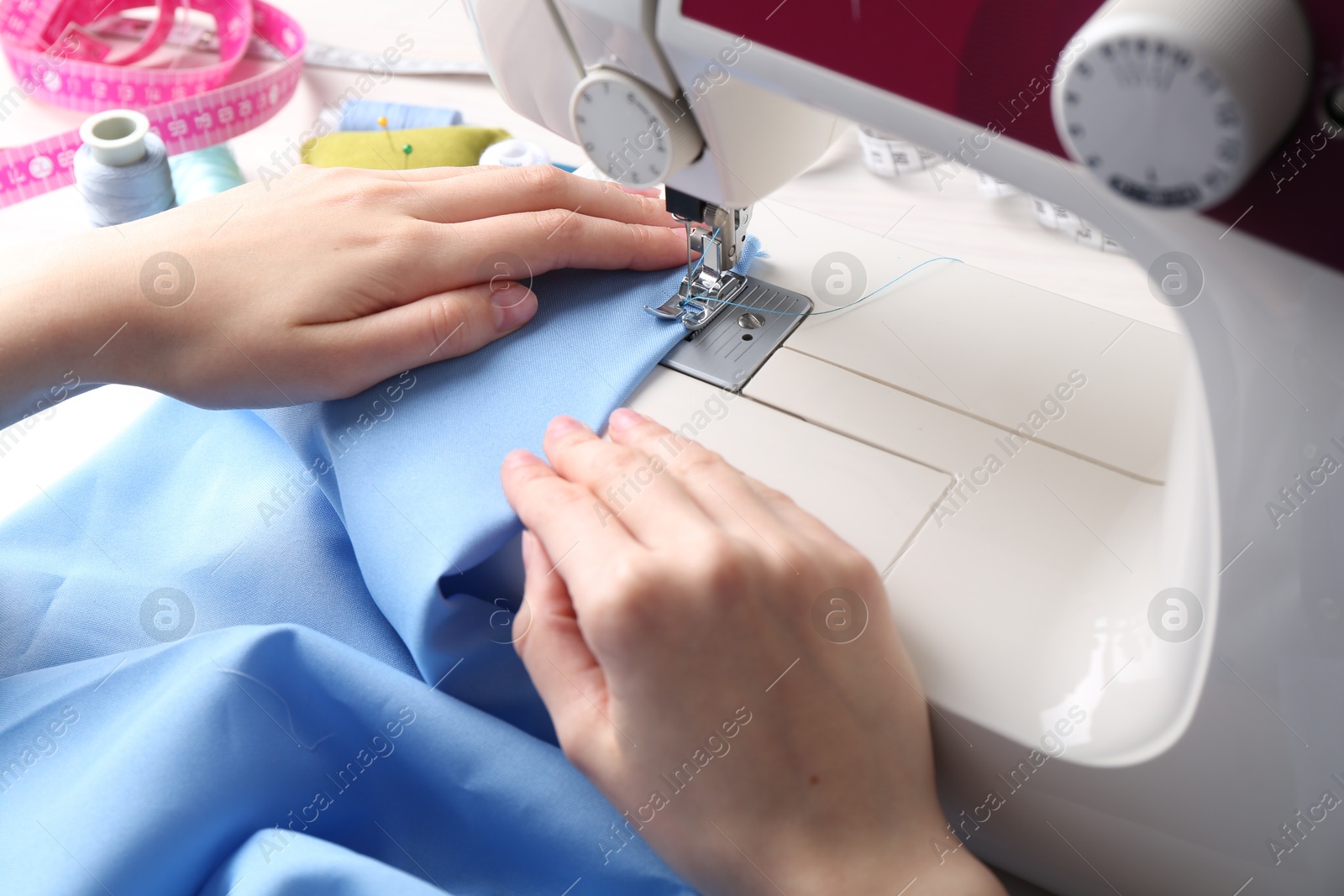 Photo of Seamstress working with sewing machine at table indoors, closeup