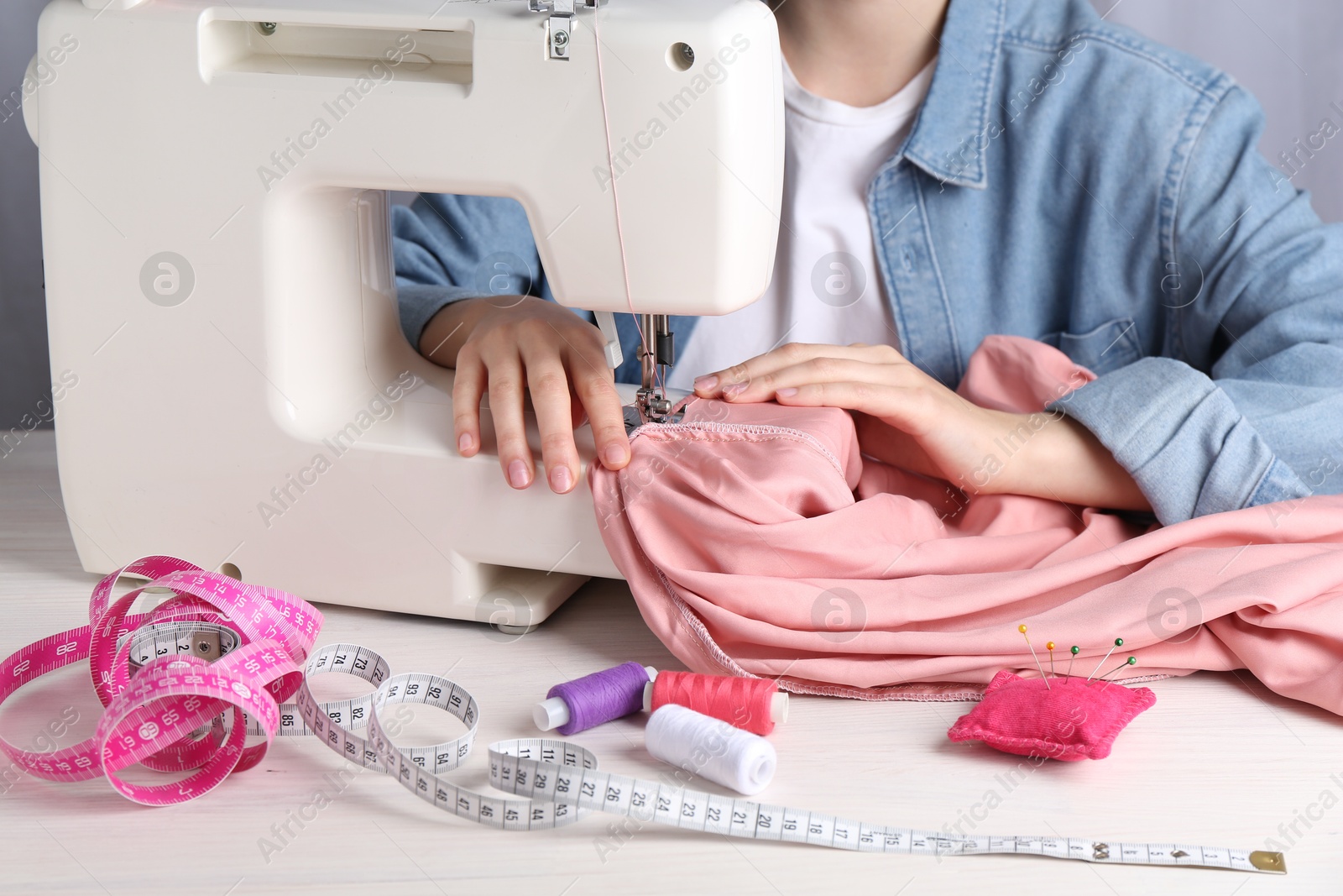 Photo of Seamstress working with sewing machine at white table indoors, closeup