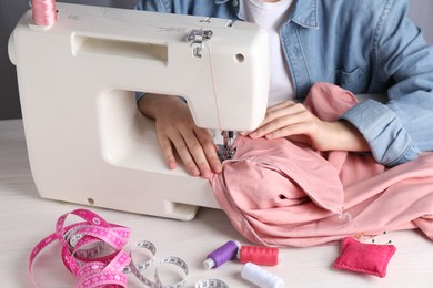 Photo of Seamstress working with sewing machine at white wooden table indoors, closeup