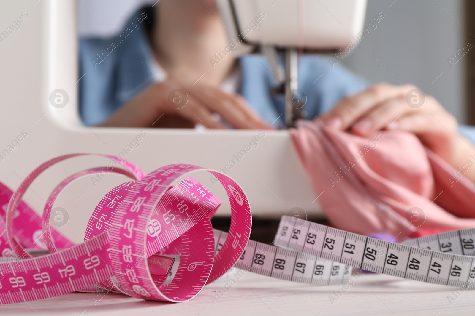 Photo of Seamstress working with sewing machine at white table indoors, selective focus