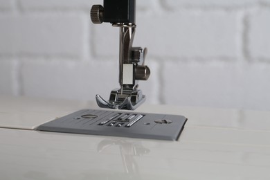 Photo of Modern sewing machine against white brick wall, closeup