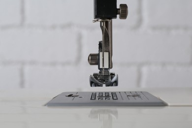 Modern sewing machine against white brick wall, closeup