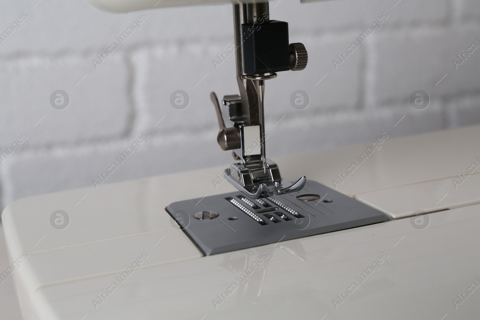 Photo of Modern sewing machine against white brick wall, closeup