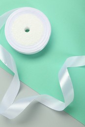 Beautiful white ribbon reel on color background, top view