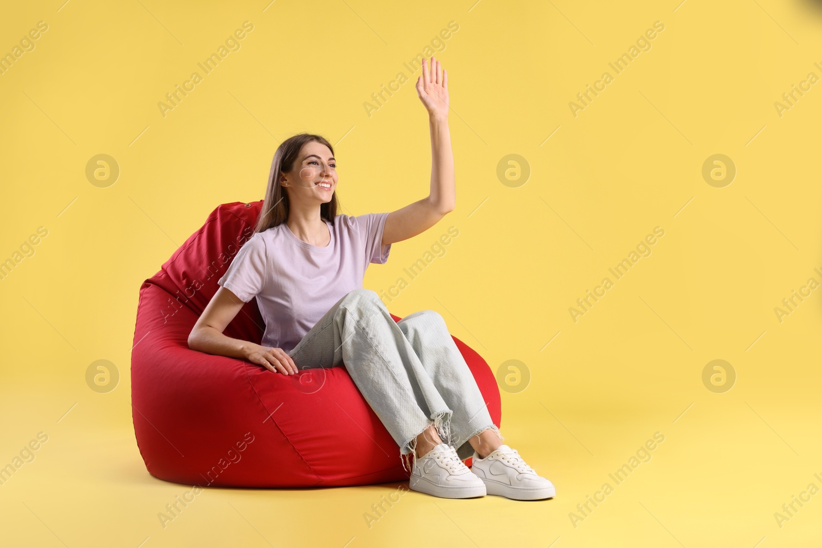 Photo of Smiling woman sitting on red bean bag chair against yellow background, space for text