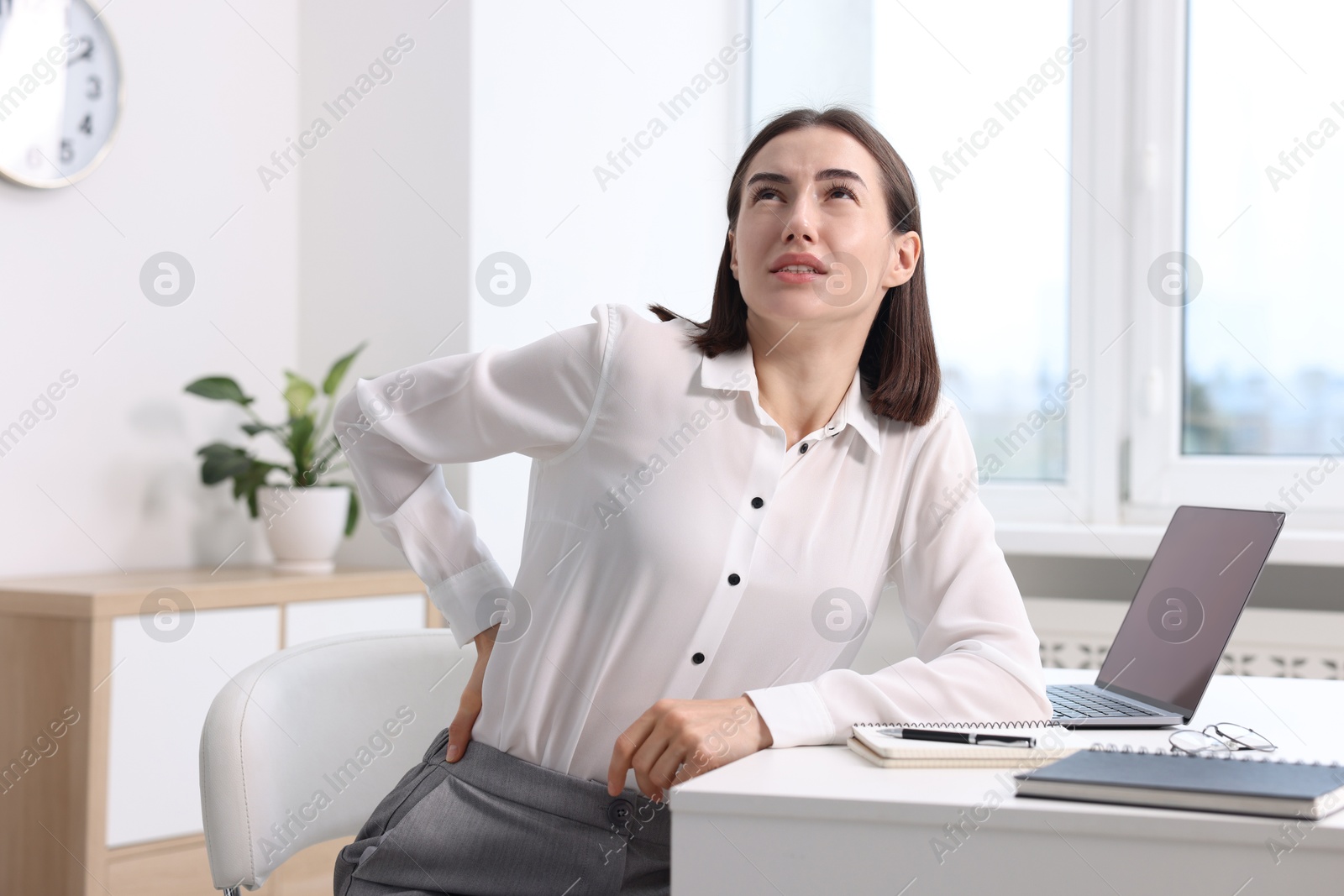 Photo of Woman suffering from back pain in office. Symptom of poor posture