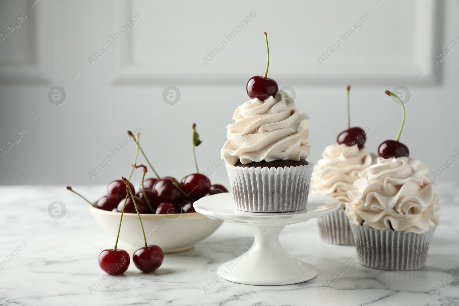 Photo of Delicious cupcakes with cream and cherries on white marble table