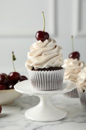 Photo of Delicious cupcakes with cream and cherries on white marble table