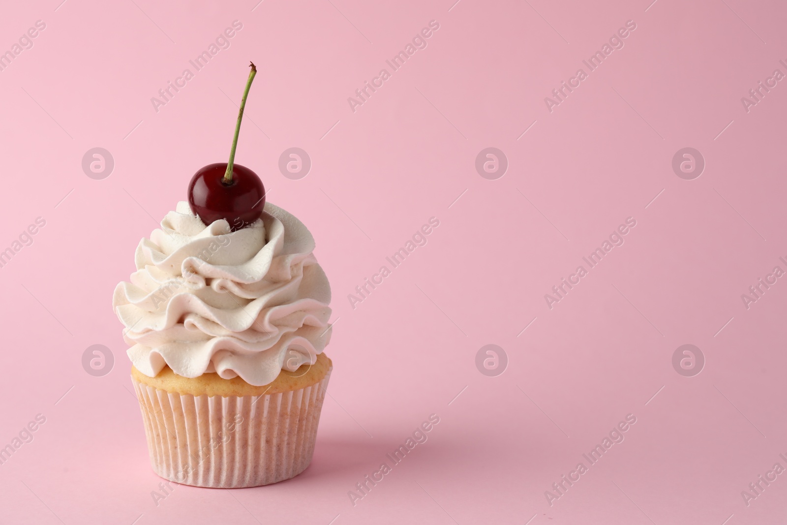 Photo of Delicious cupcake with cream and cherry on pink background, space for text