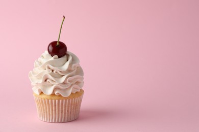 Delicious cupcake with cream and cherry on pink background, space for text