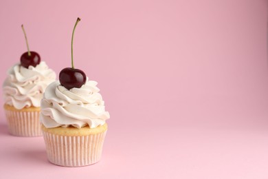 Delicious cupcakes with cream and cherries on pink background, space for text