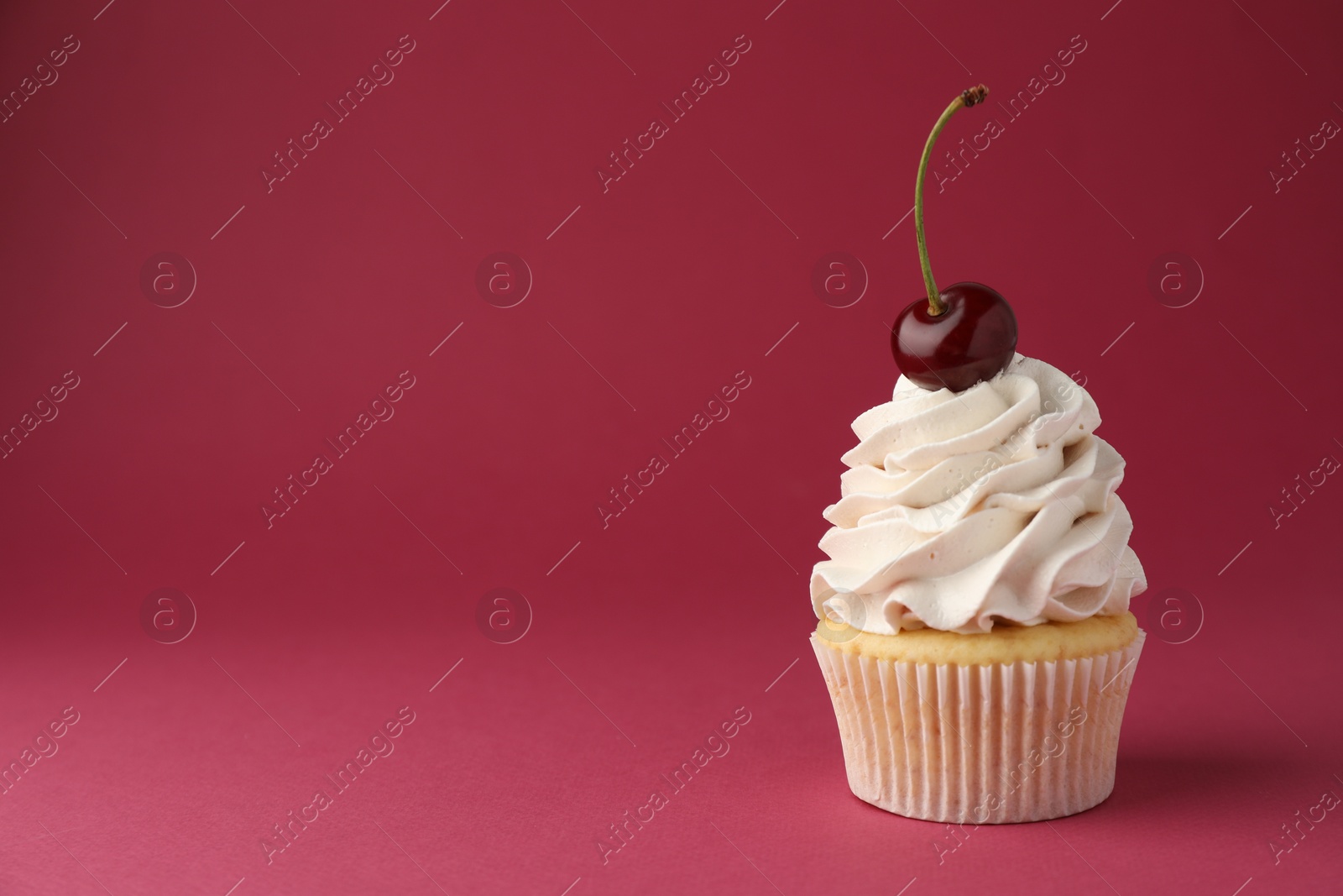 Photo of Delicious cupcake with cream and cherry on red background, space for text