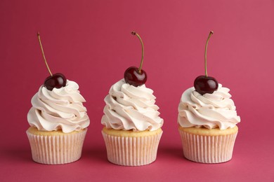 Photo of Delicious cupcakes with cream and cherries on red background