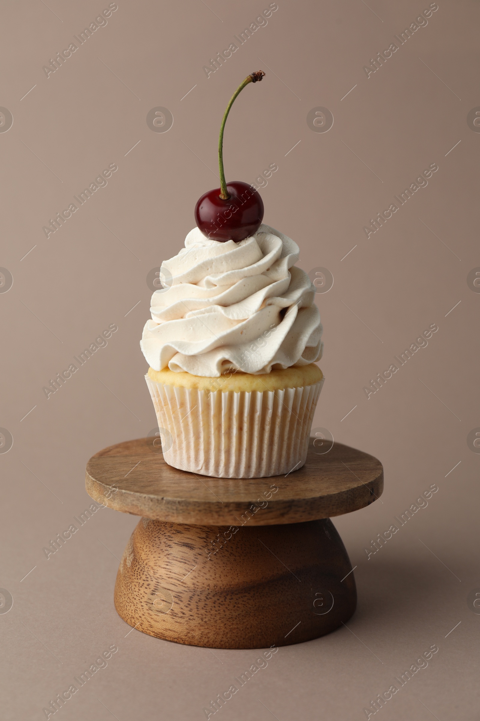 Photo of Delicious cupcake with cream and cherry on dark beige background