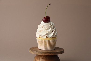 Delicious cupcake with cream and cherry on dark beige background