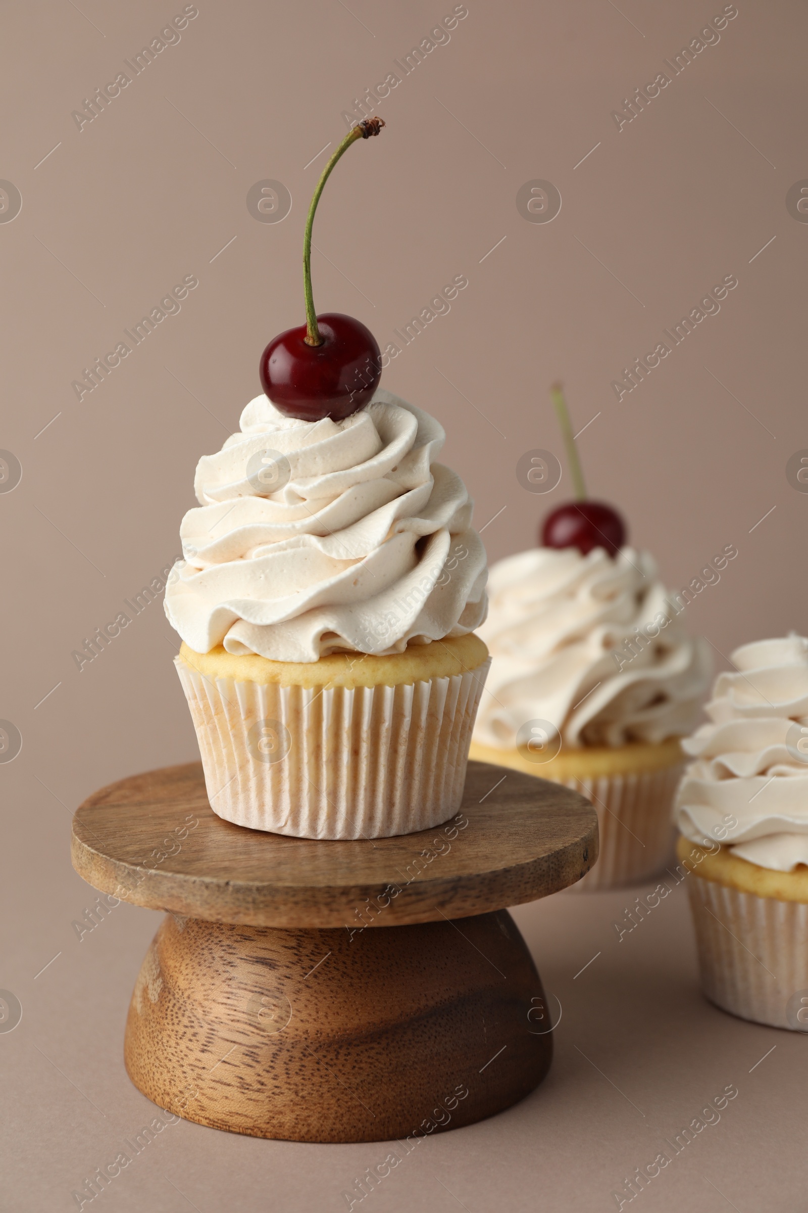 Photo of Delicious cupcakes with cream and cherries on dark beige background