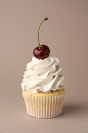 Photo of Delicious cupcake with cream and cherry on dark beige background