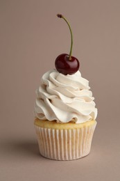 Photo of Delicious cupcake with cream and cherry on dark beige background