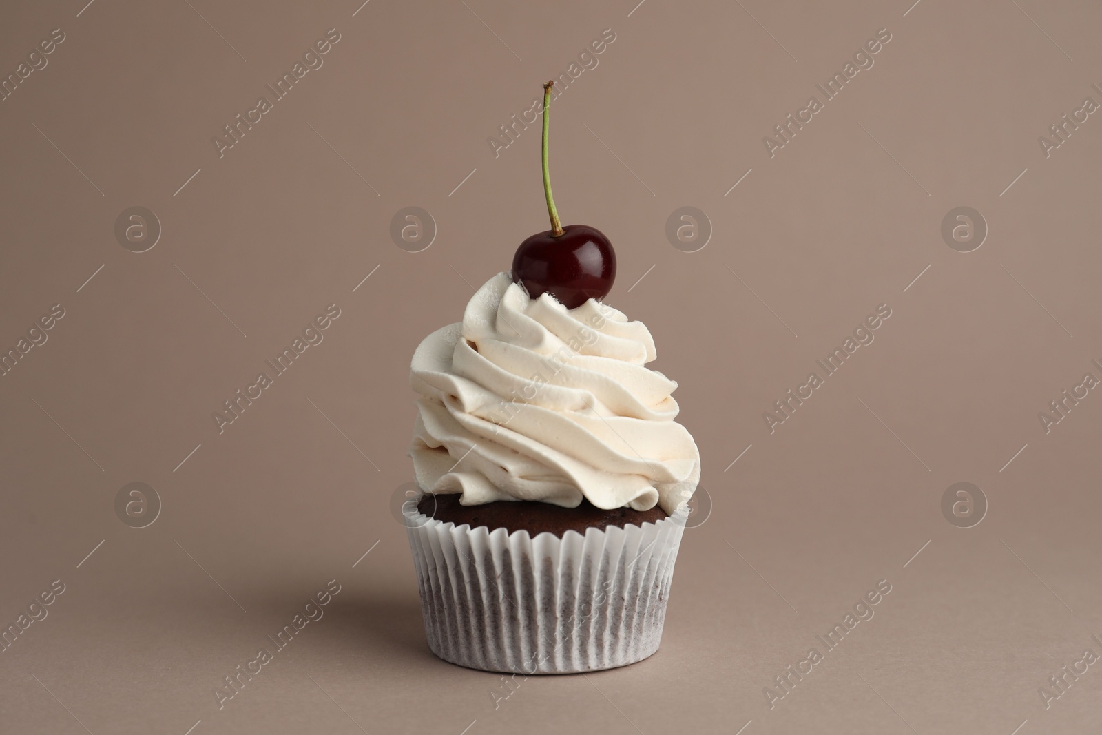 Photo of Delicious cupcake with cream and cherry on dark beige background