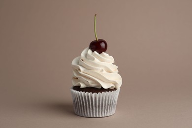 Photo of Delicious cupcake with cream and cherry on dark beige background