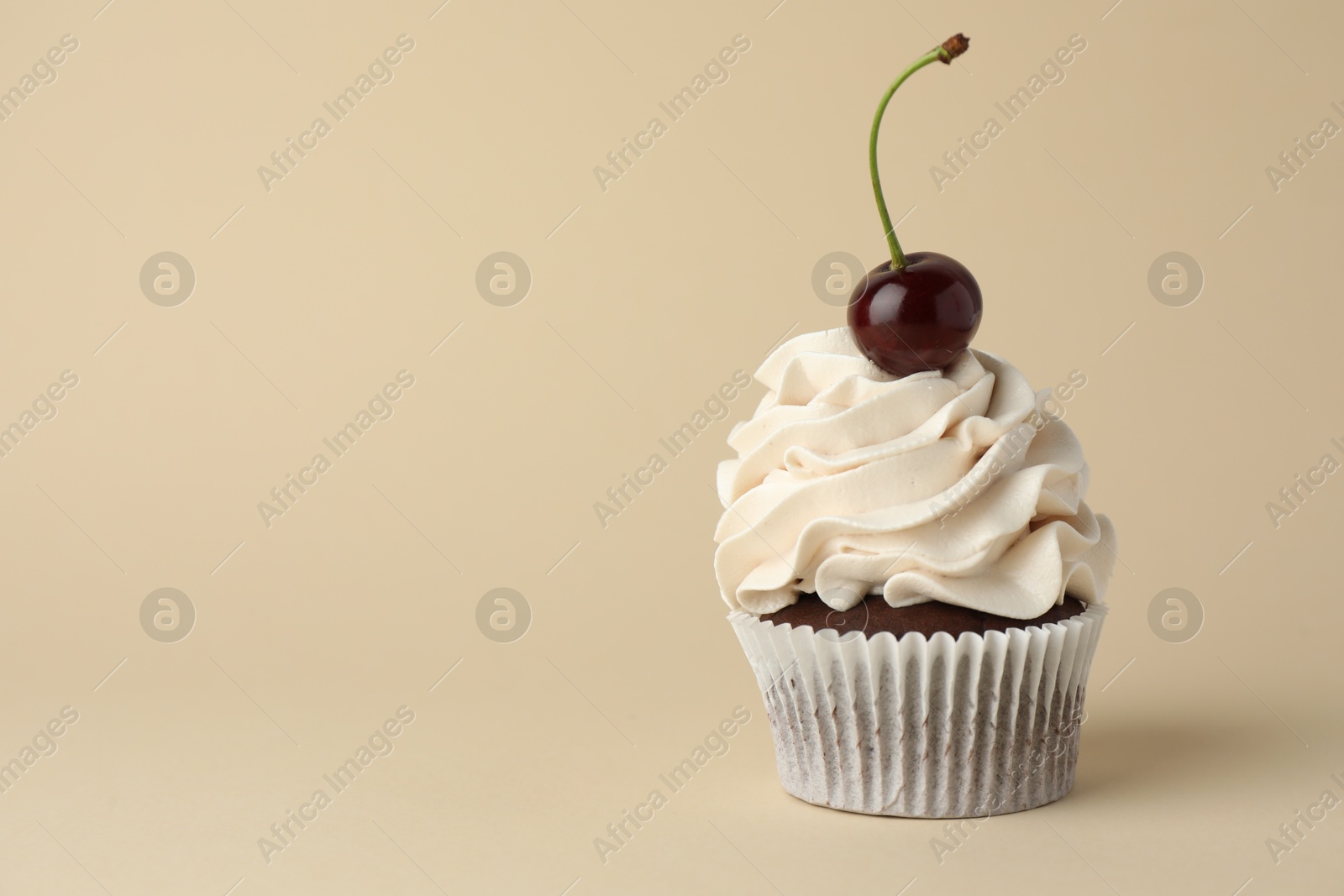 Photo of Delicious cupcake with cream and cherry on beige background, space for text