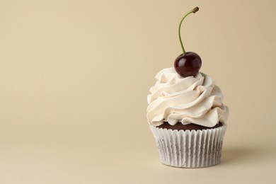 Delicious cupcake with cream and cherry on beige background, space for text