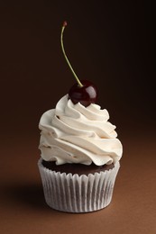 Photo of Delicious cupcake with cream and cherry on brown background