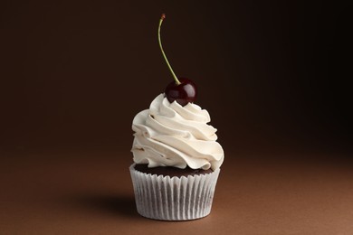 Photo of Delicious cupcake with cream and cherry on brown background