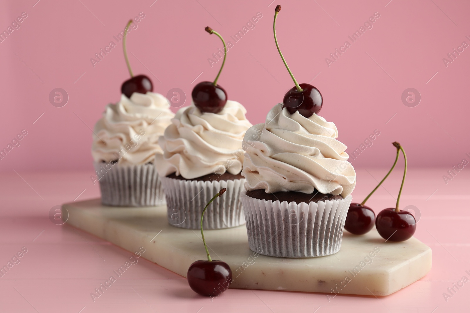 Photo of Delicious cupcakes with cream and cherries on pink table