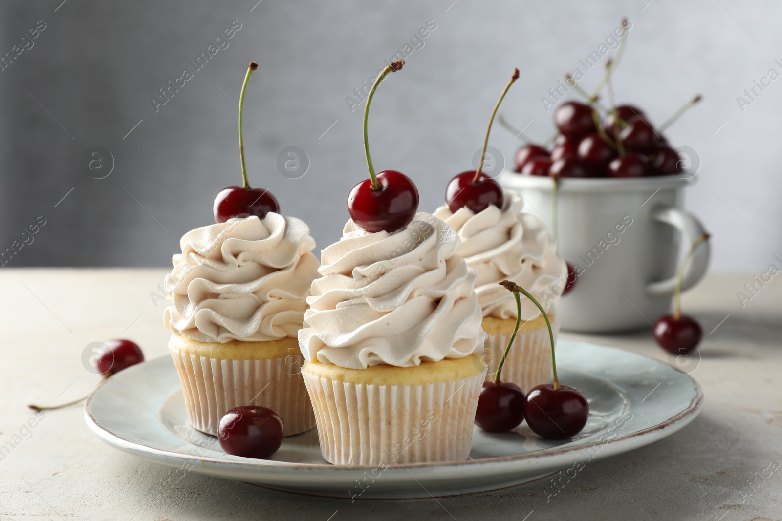 Photo of Delicious cupcakes with cream and cherries on light textured table, closeup