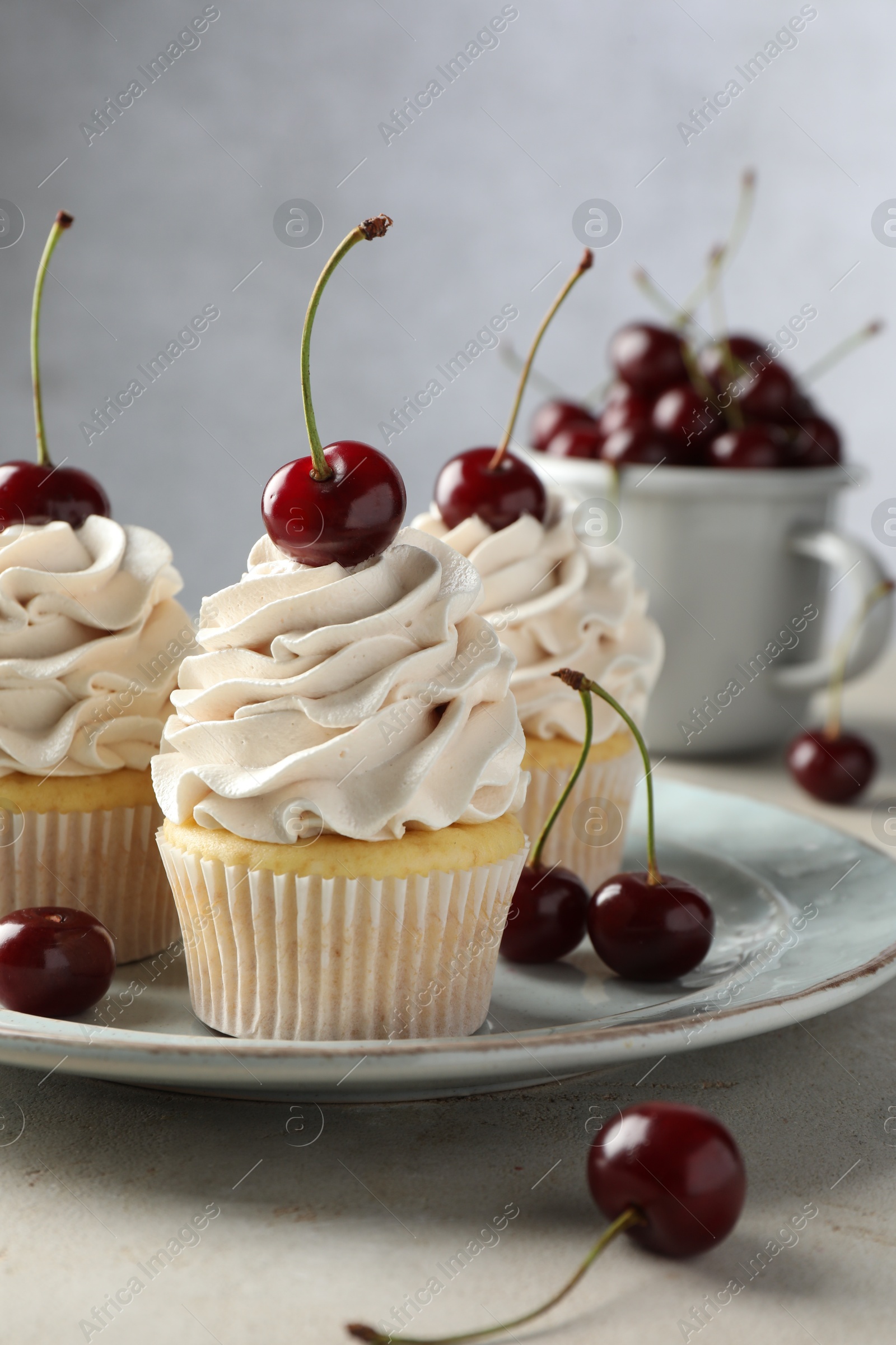 Photo of Delicious cupcakes with cream and cherries on light textured table, closeup